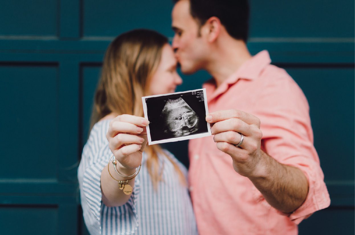 a smiling couple holding an ultrasound photo