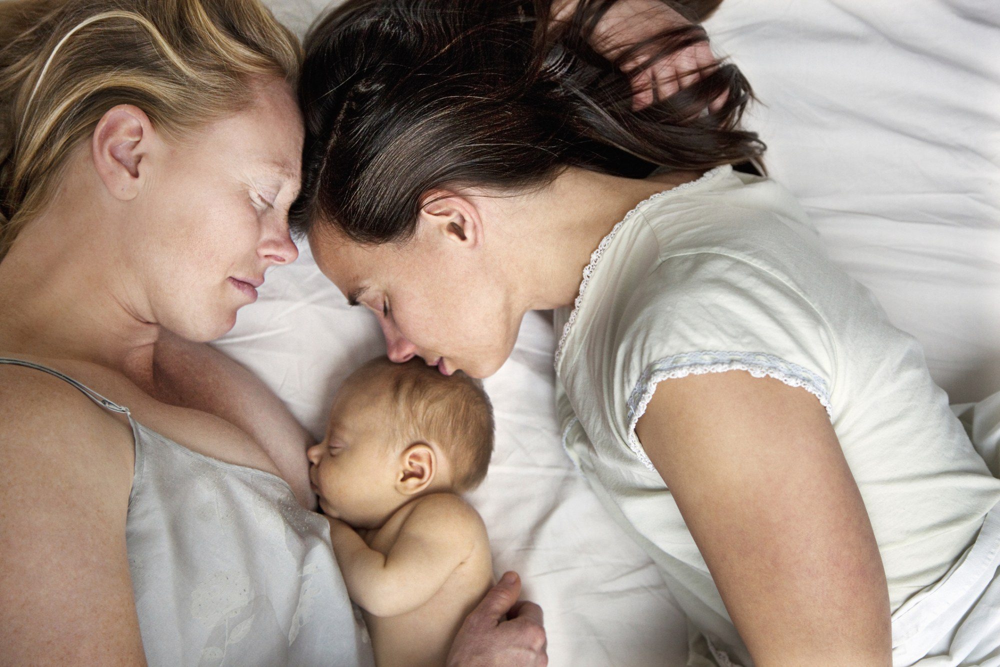 lesbian couple snuggling with sleeping baby